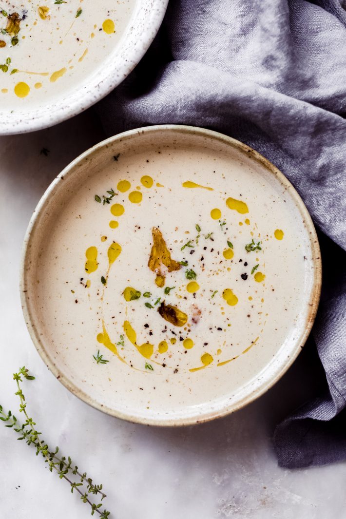 roasted cauliflower soup in speckled bowl topped with truffle oil and fresh thyme leaves