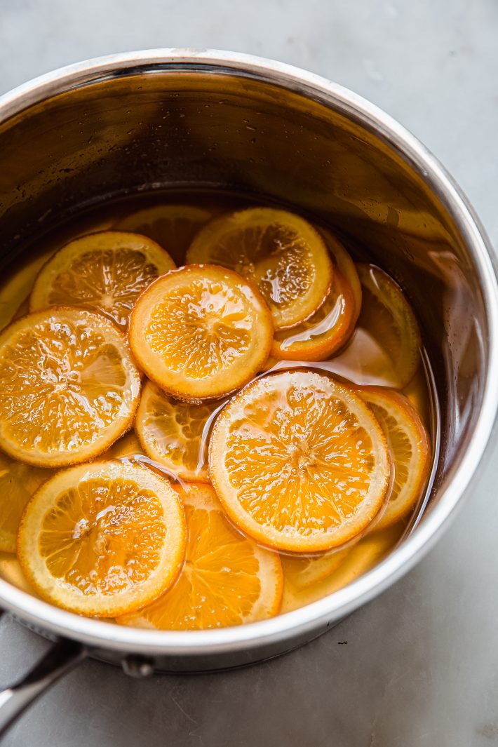 orange slices being candied in syrup in saucepan