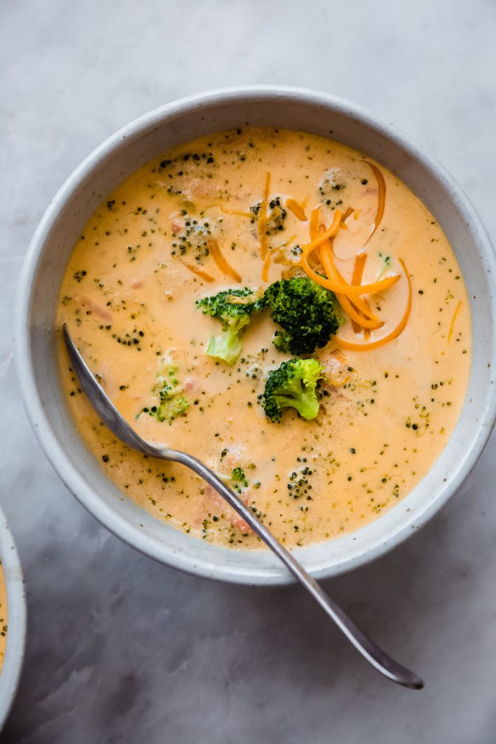 bowl of keto broccoli cheese soup with spoon on white marble