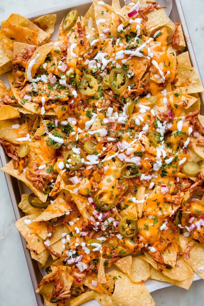 sheet pan with prepared nachos drizzled in sour cream