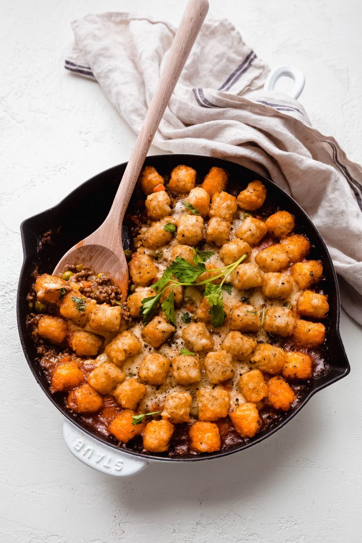 wooden spoon lifting filling in skillet with potato puffs