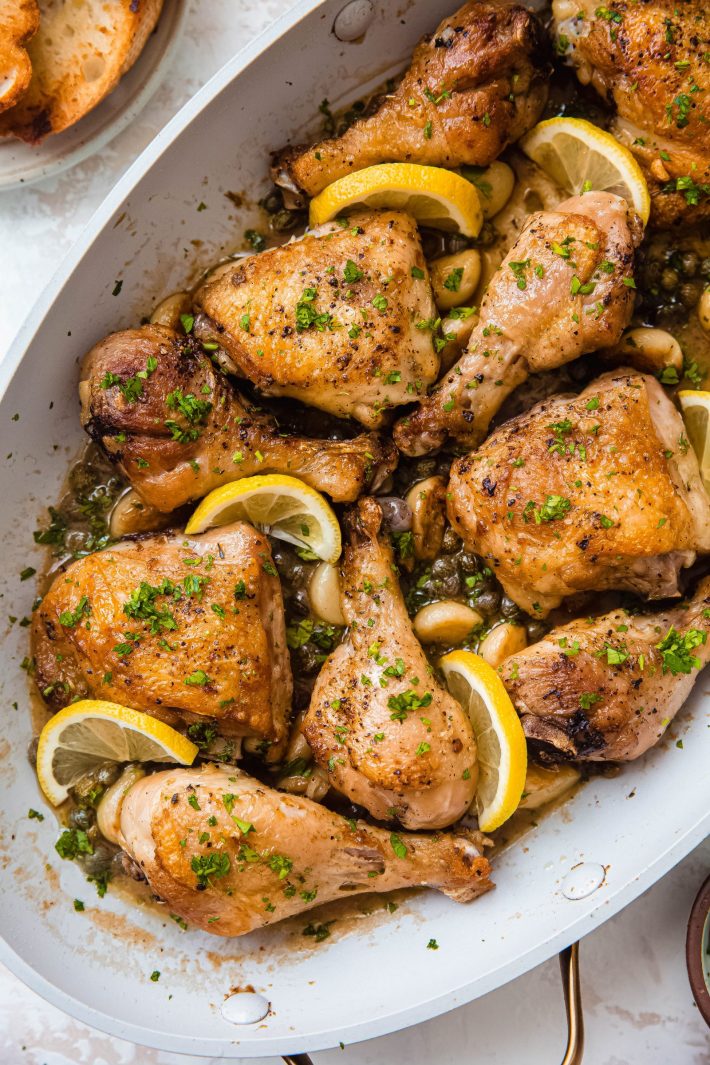 braiser showing chicken legs and thighs topped with chopped parsley and lemon slices