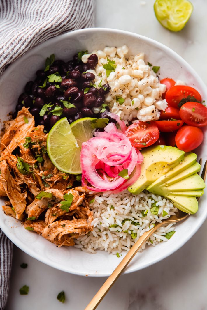 Chicken Tinga bowl topped with black beans, corn, tomatoes, pickled onions, and avocados