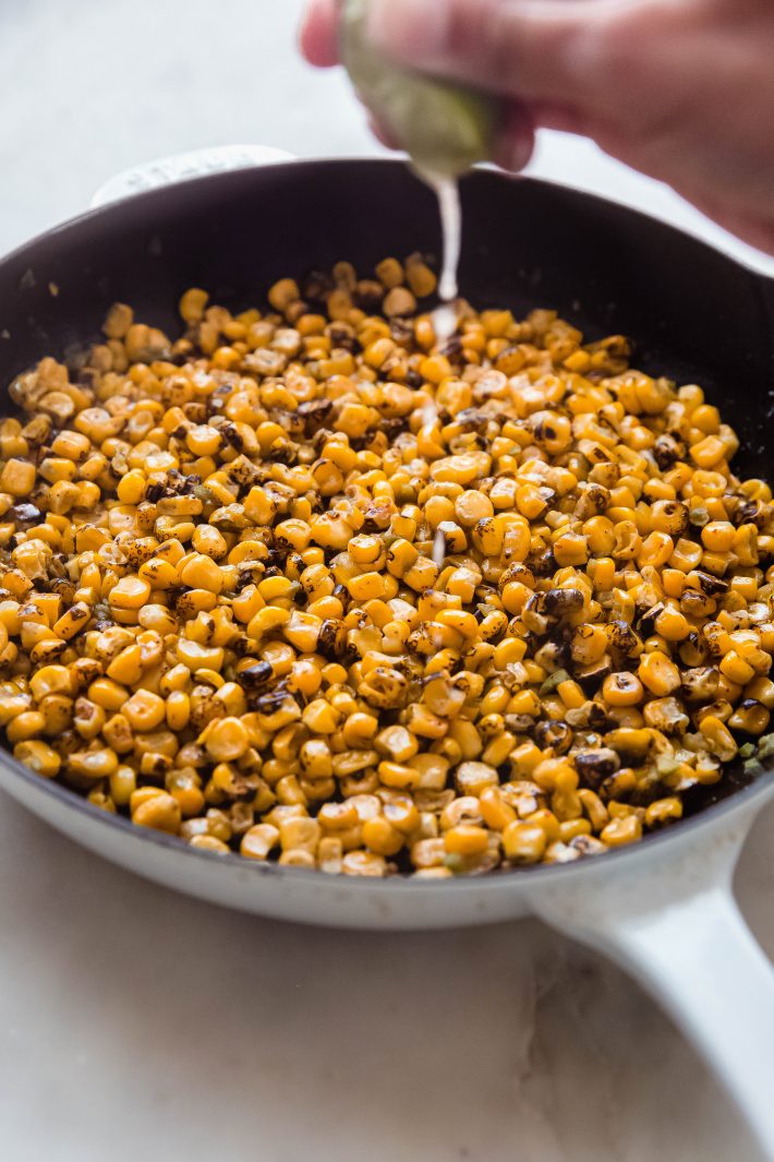 hand squeezing lime juice on fire-roasted corn in skillet