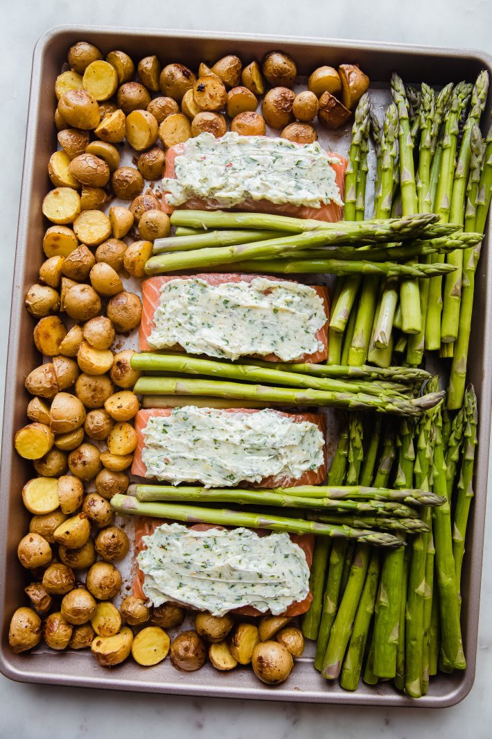 sheet pan with butter compound salmon, potatoes and asparagus before baking