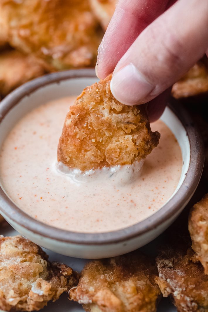 hand dipping fried pickle in remoulade 
