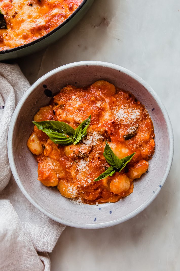 bowl of gnocchi in pomodoro topped with grated parmesan and fresh basil