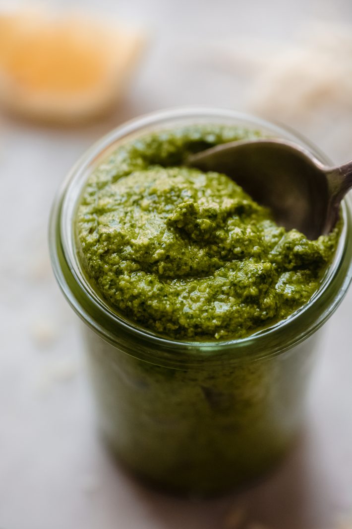 spinach pesto being lifted from glass jar with spoon