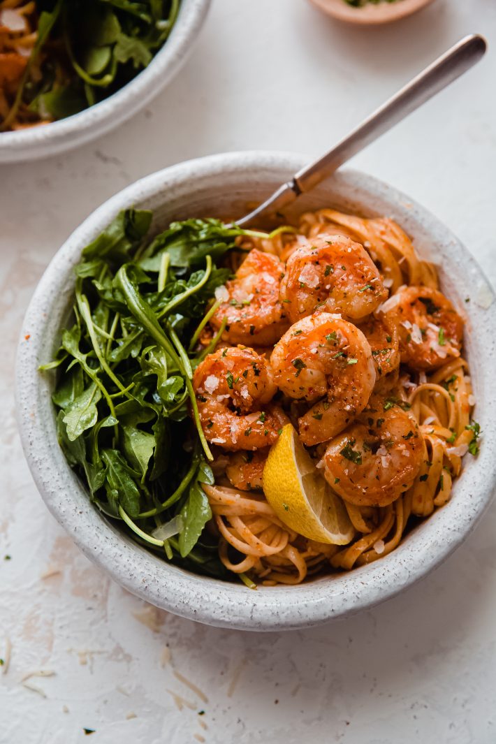 bowl with pasta topped with shrimp and arugula on the side