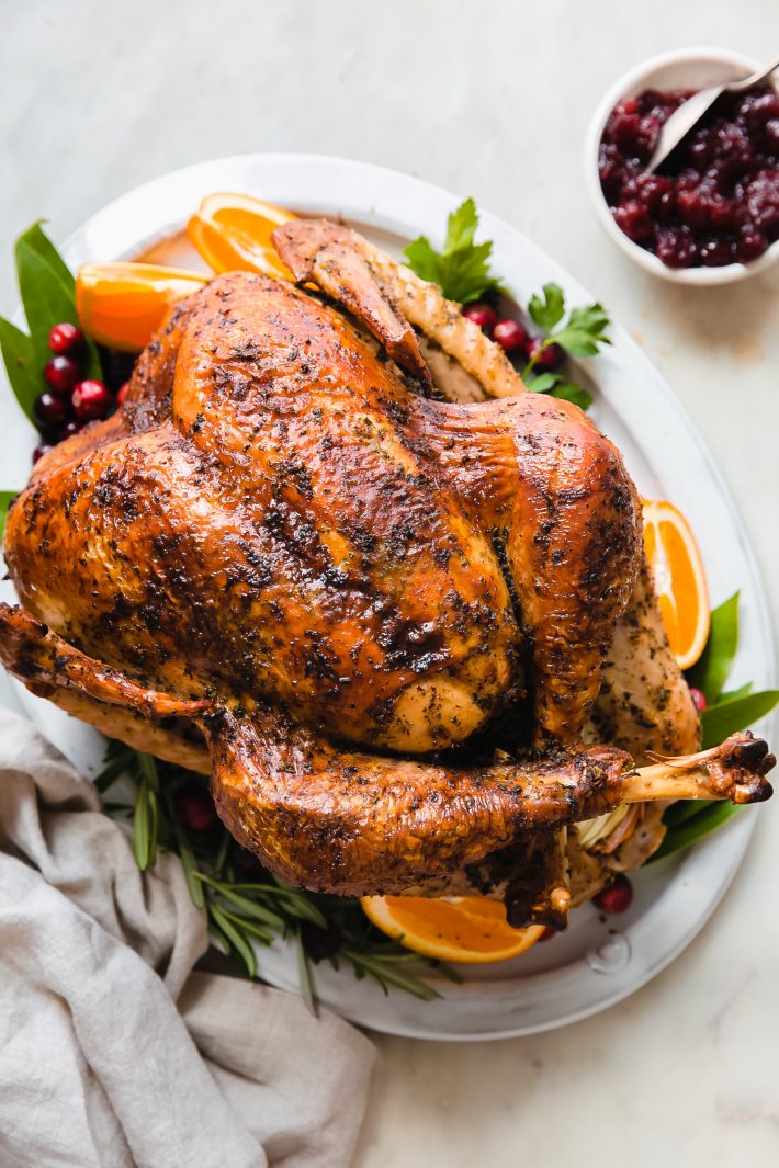 thanksgiving turkey surrounded by herbs, oranges, and cranberries