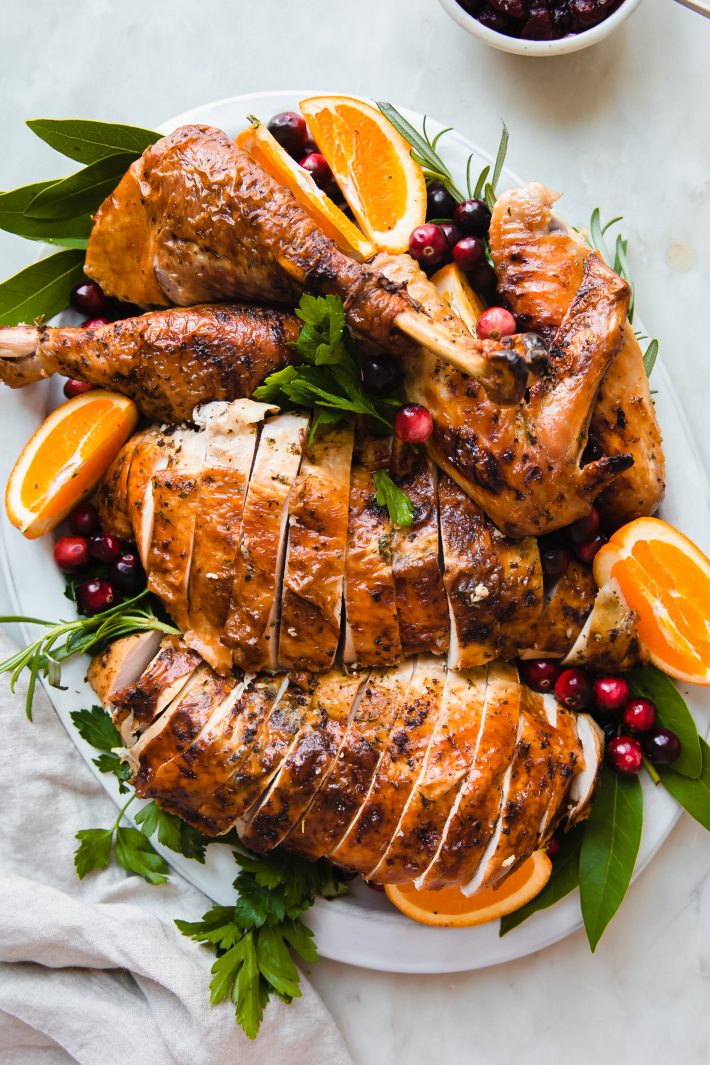 cut up thanksgiving turkey on platter with oranges, cranberries, and herbs