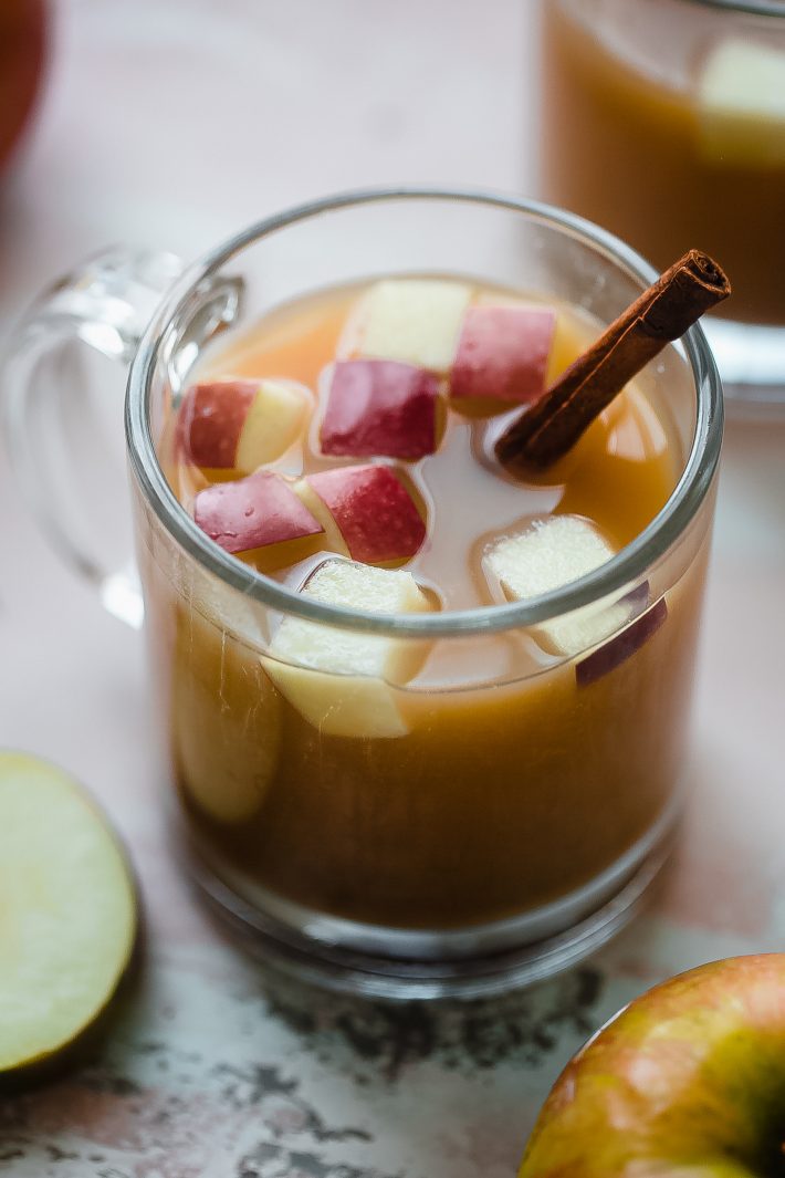 cider in glass with cinnamon sticks surrounded by apples