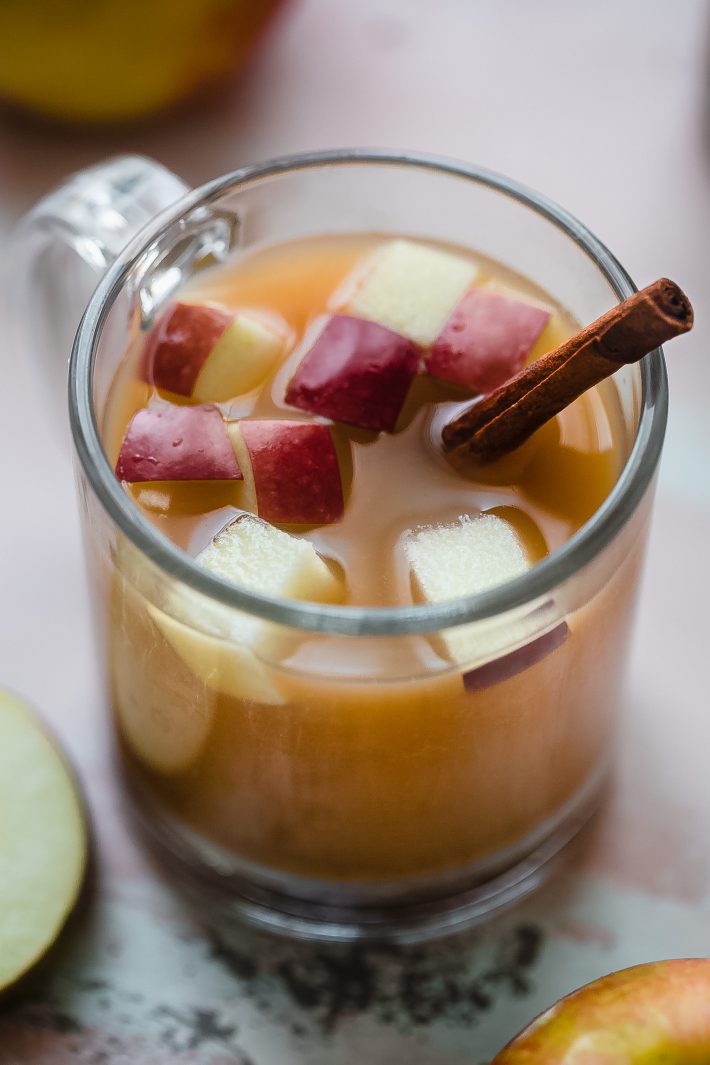 apple cider in clear glass with chunks of apples and cinnamon stick