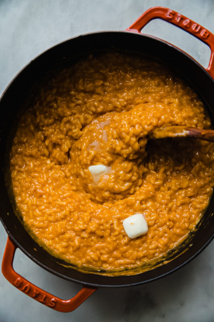 squash risotto in cast iron pot with butter being stirred in