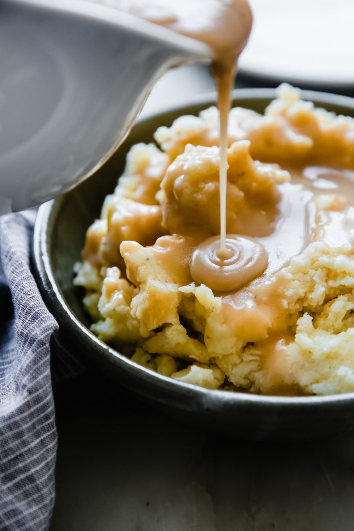gravy pouring from gravy boat over mashed potatoes