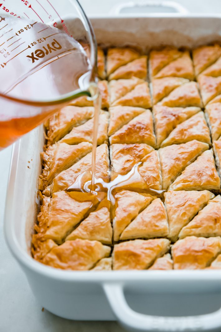 pouring simple syrup over baklava triangles