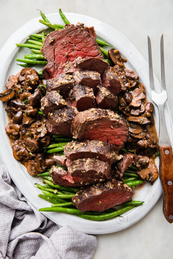 sliced beef tenderloin on plate with green beans and mushroom pan sauce
