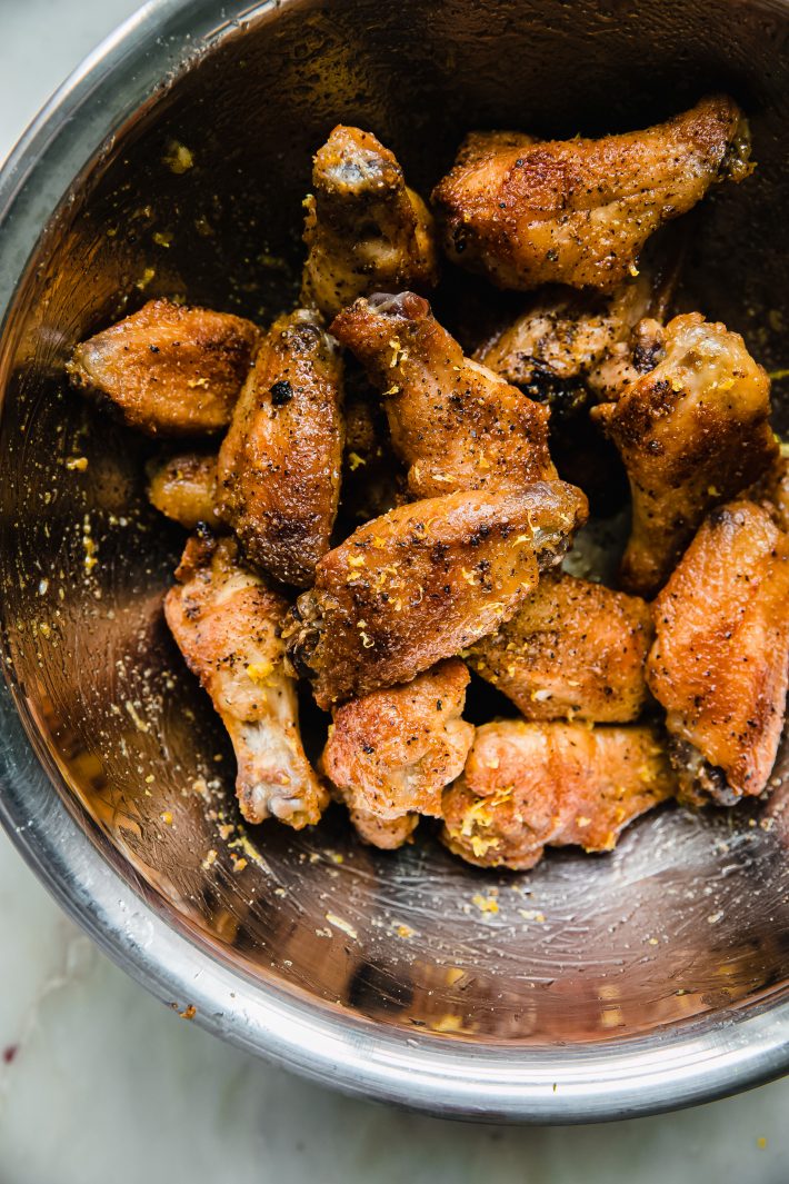 chicken wings tossed with lemon pepper butter sauce in metal bowl