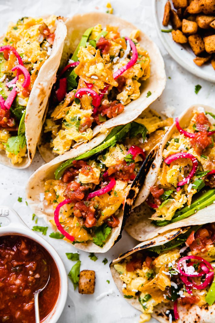 scattered filled Migas tacos on parchment with potatoes and salsa