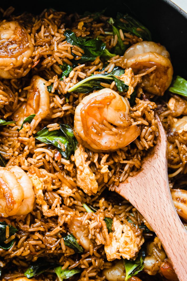 wooden spoon holding fried rice, basil, and shrimp