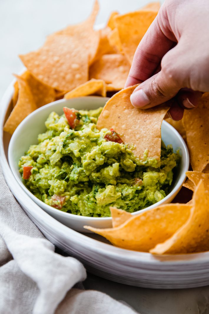 hand dipping tortilla chip in guacamole