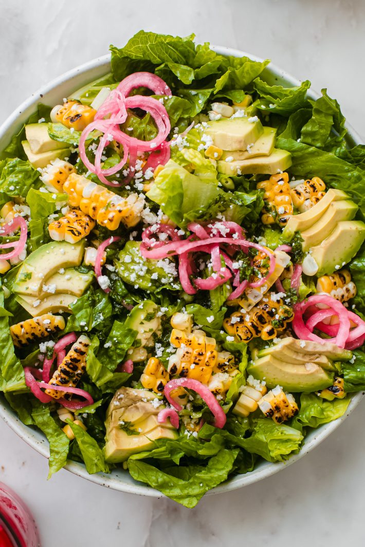 charred corn on romaine lettuce with avocados pickled onions and cotija cheese