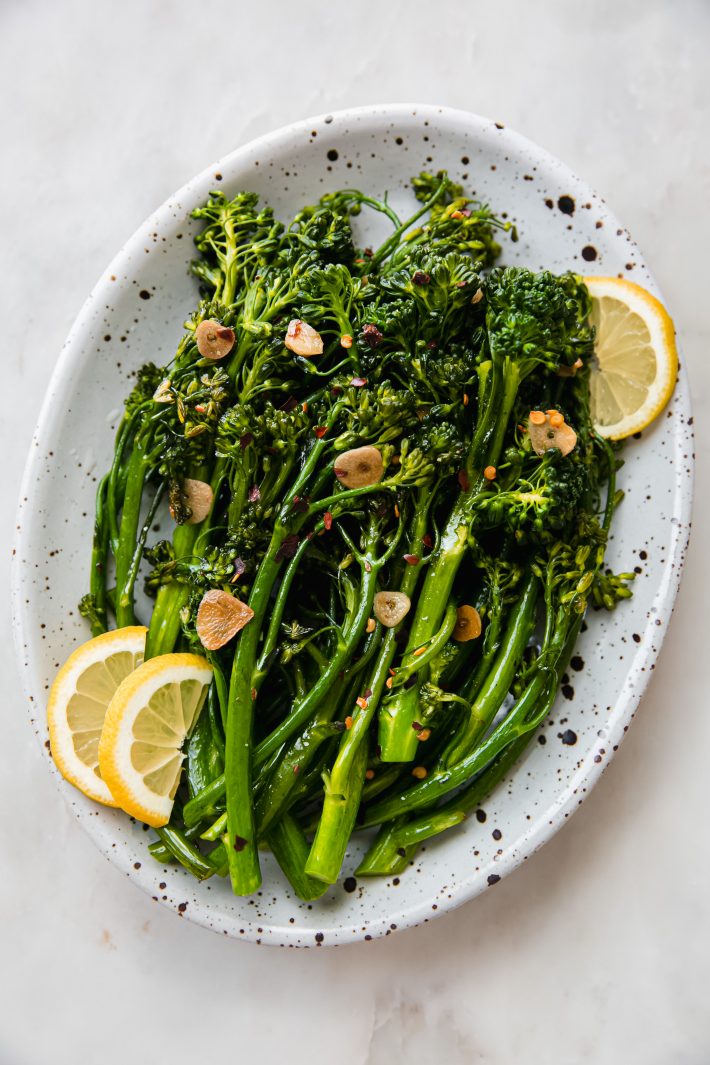 broccolini with garlic chips and lemon wedges in speckled plate