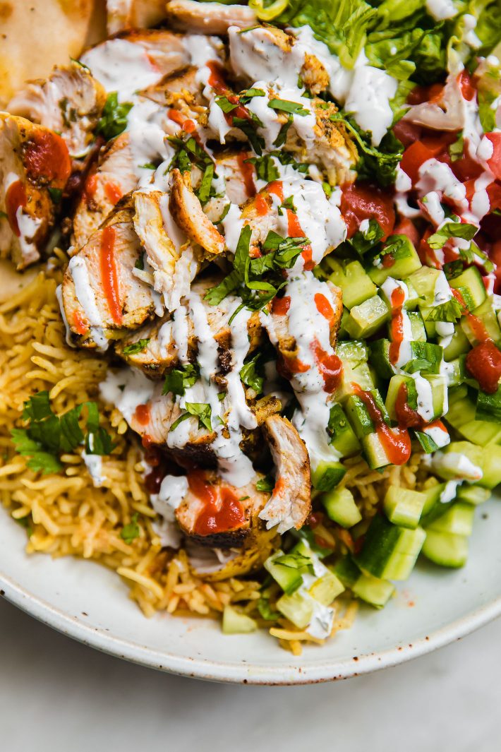 halal chicken over rice topped with cilantro white sauce and red sauce