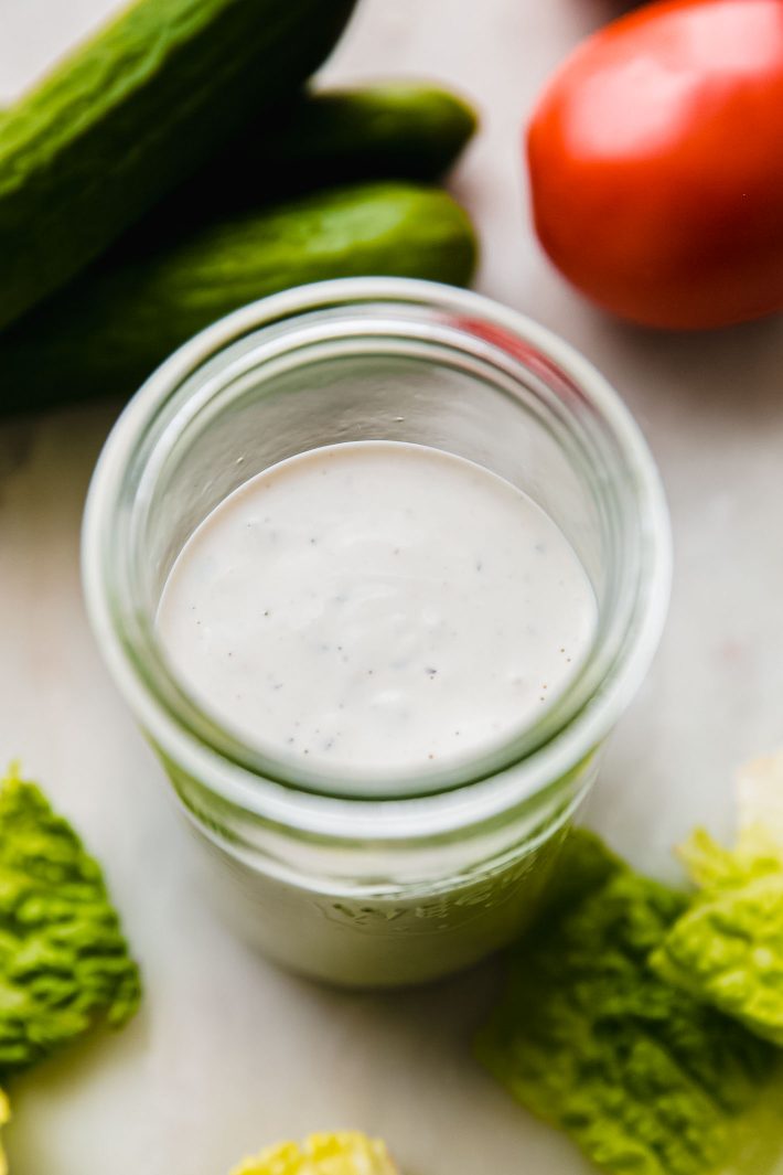 sauce in jar on white marble with veggies surrounding