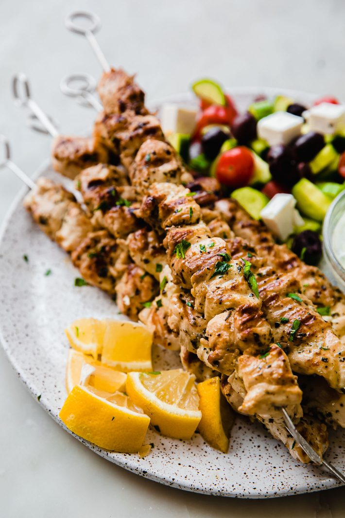 chicken souvlaki skewers on plate with lemons and greek salad