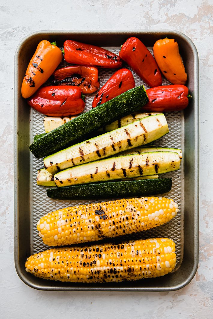 Grilled sweet peppers, zucchini spears, and corn cobs on sheet pan