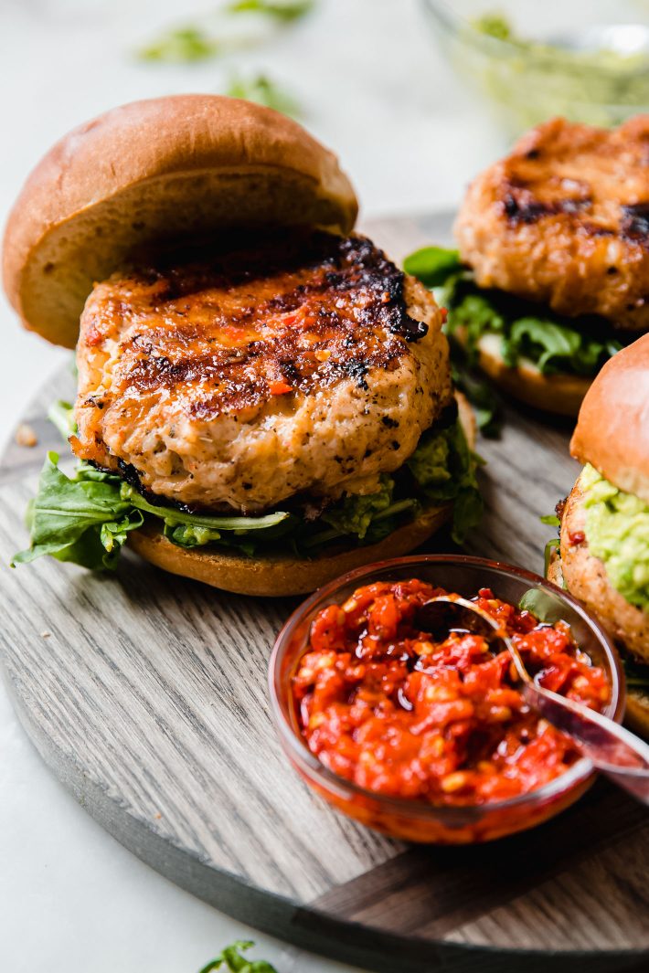 grilled chicken burgers on buns with chili sauce on wood board