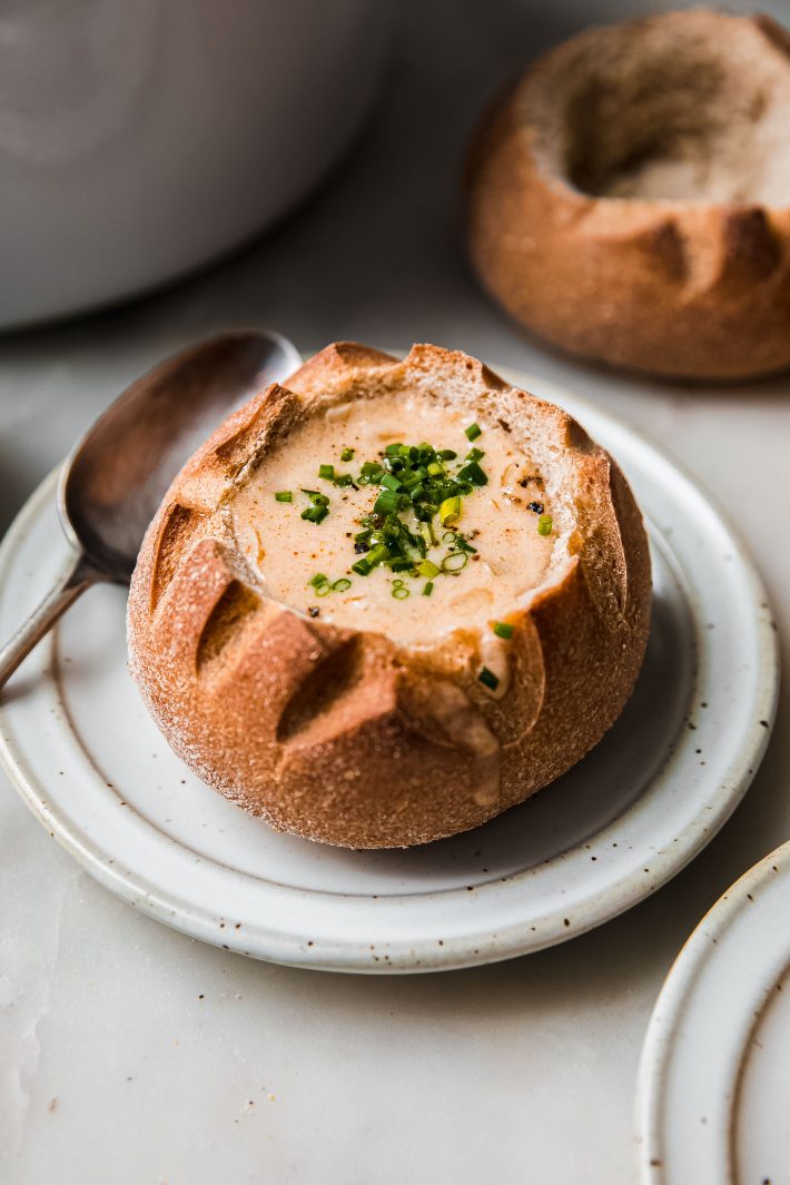 soup in bread bowl topped with chives on a plate with spoon