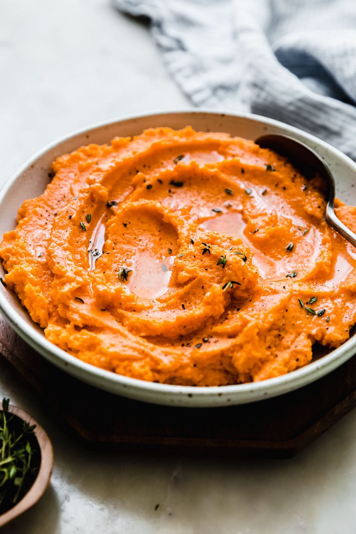 mashed sweet potatoes topped with butter, thyme, and spoon