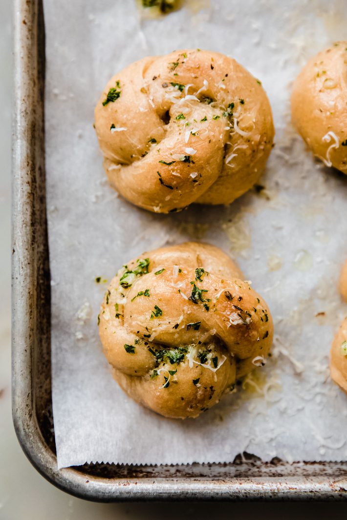 Baked knots topped with parmesan cheese on parchment