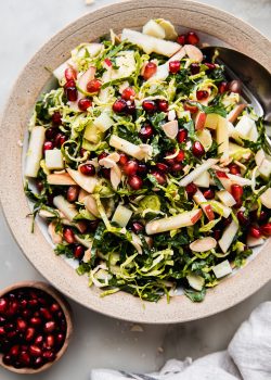 shaved brussels sprout salad in rimmed bowl with apples and pomegranate arils