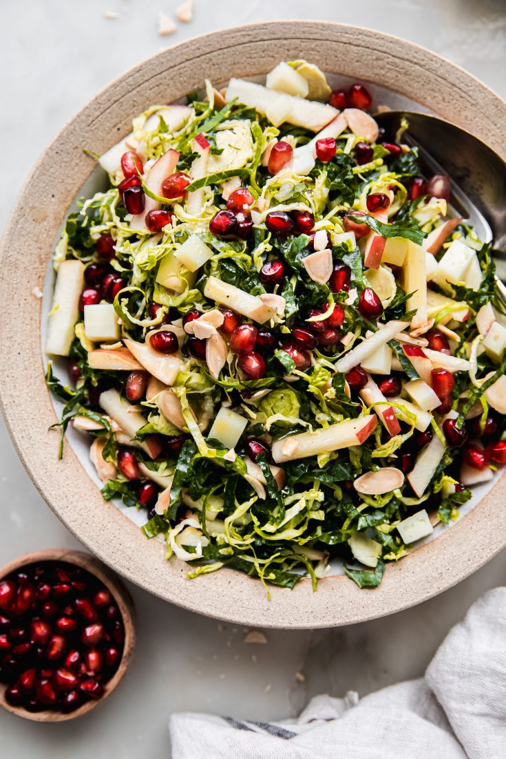 shaved brussels sprout salad in rimmed bowl with apples and pomegranate arils