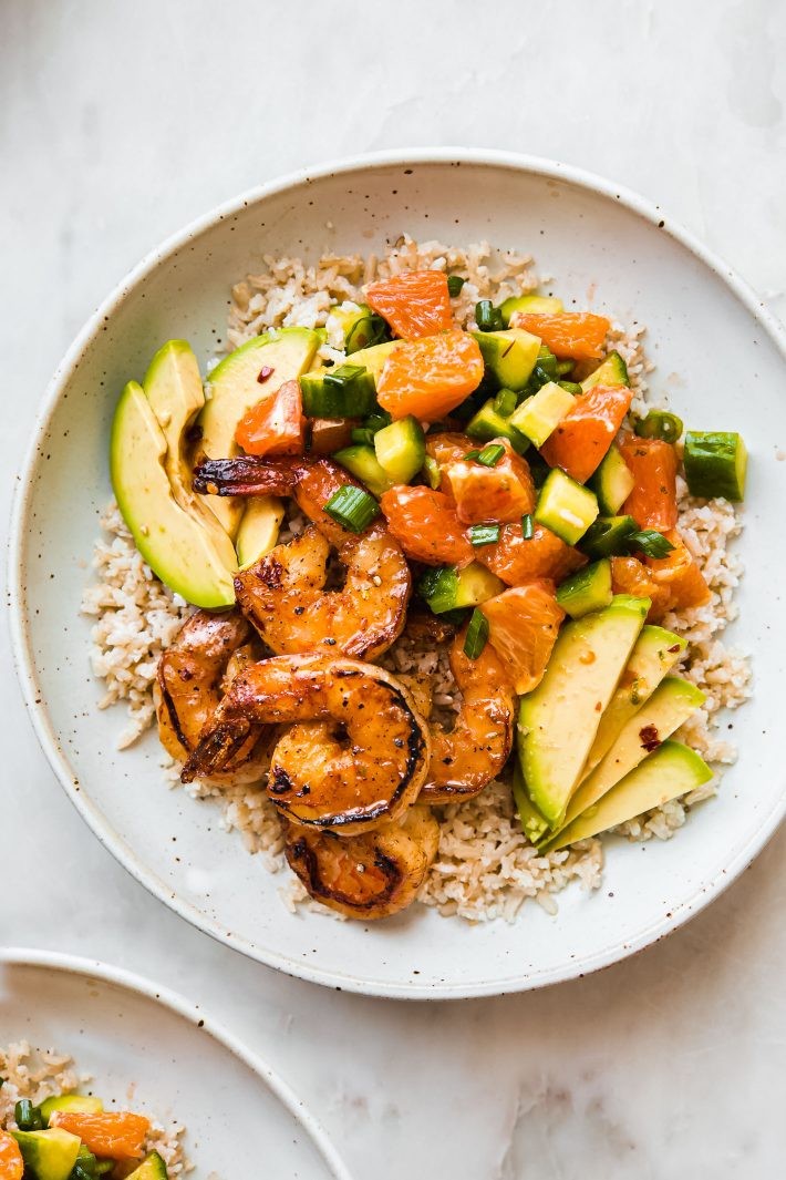 ponzu shrimp rice bowls with avocado and orange cucumber salad in speckled plate