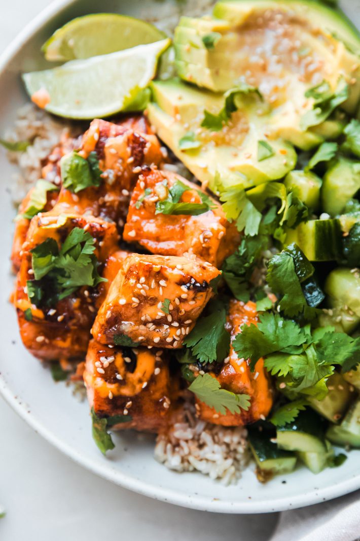 salmon bowl with sesame seeds and honey, lime wedges, cilantro, avocado, and cucumbers