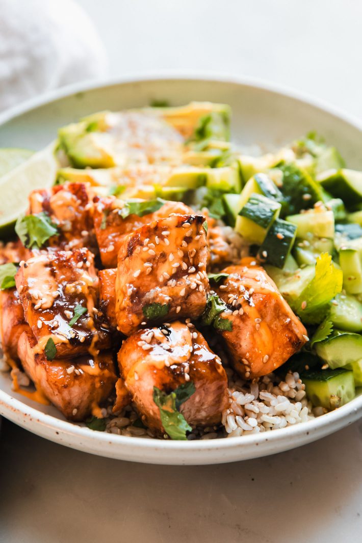 salmon pieces covered with spicy mayo and sesame seeds with cucumbers and rice