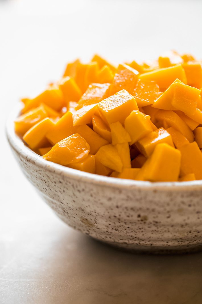 chopped mango chunks in speckled bowl on white marble